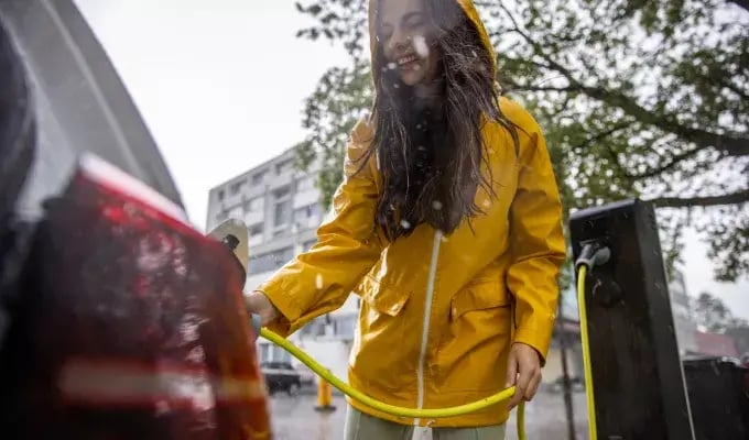 Frau lädt ihr E-Auto im Regen